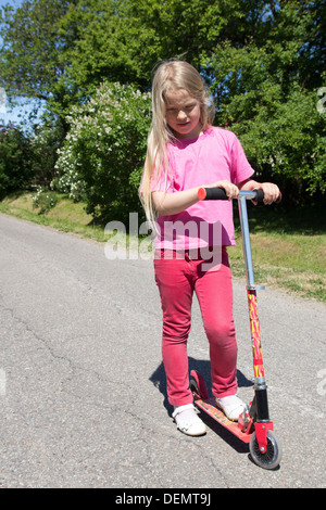little girl rides a scooter on a rural road Stock Photo