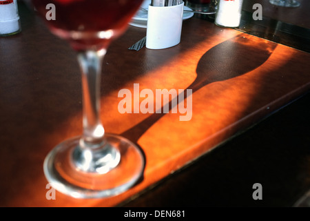 A wine glass full of red wine casting a long shadow on a dining table. Stock Photo