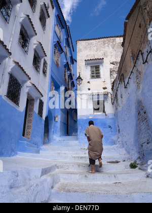 Person walking away on a street with blue painted houses in Chefchaouen, Morocco Stock Photo