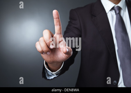 Businessman pressing an imaginary button on bokeh over dark background Stock Photo