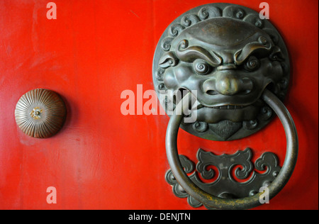 An ornate door knocker in the shape of a fierce warrior on the front of a studded red door. Stock Photo