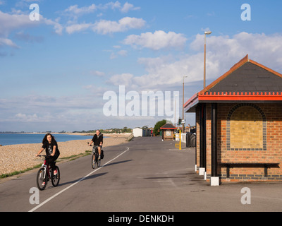 Two people cycling along cycle track for exercise on a seafront promenade in Aldwick, Bognor Regis, West Sussex, England, UK, Britain Stock Photo