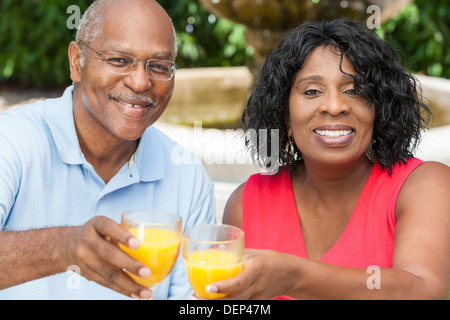 A happy, smiling man and woman senior African American couple outside drinking orange juice Stock Photo