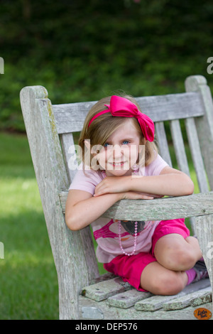 Young female Caucasian child posing in a park on a rustic bench. Stock Photo