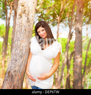 Portrait of expectant arabic female outdoors, spending time in garden in summer time, touching belly Stock Photo