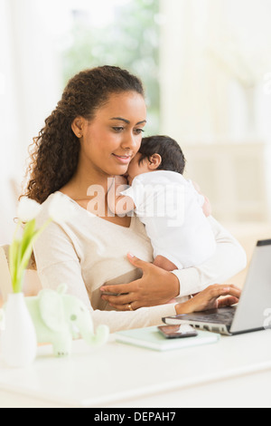 Hispanic mother using laptop and holding infant son Stock Photo