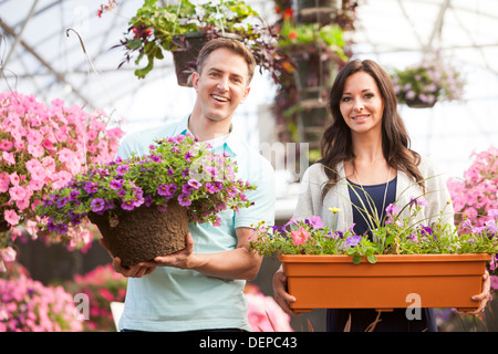 Caucasian couple carrying potted flowers in plant nursery Stock Photo
