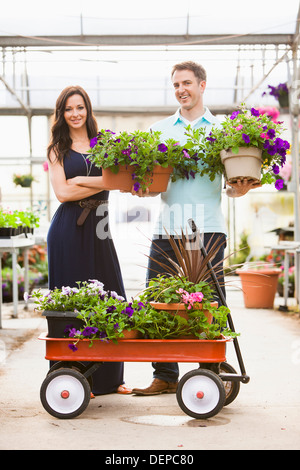 Caucasian couple carrying potted flowers in plant nursery