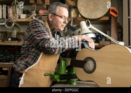 Guitar maker finishing acoustic guitar in workshop Stock Photo