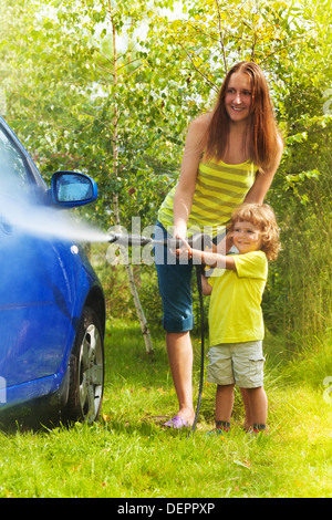 Mother and three years old son washing car with high pressure washer with boy pointing water nozzle  Stock Photo