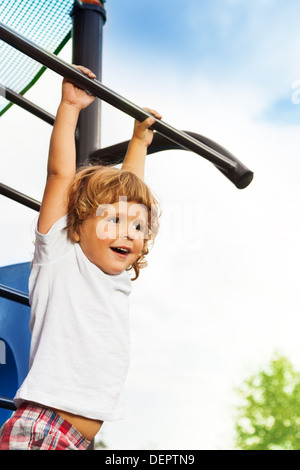 Close portrait of happy three years old boy about to hand on the horizontal bar on playground Stock Photo