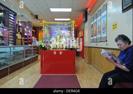 A Buddhist shrine in a store front on Mott Street in Manhattan's Chinatown. Worshippers leave offerings of oranges and money. Stock Photo