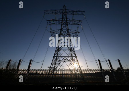 The sun sets behind an enormous electricity pylon Stock Photo