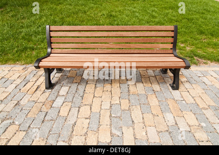 Wooden bench in the park in front of the grass lawn. Stock Photo