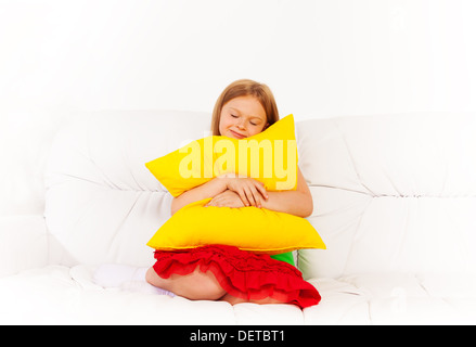 One happy calm sleepy and relaxed girl 6 years old sitting with pillow on the white leather coach Stock Photo