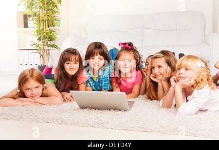 Group of happy little kids, boys and girls laying on the floor with laptop in living room Stock Photo