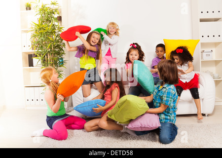 Pillow fight - large group of kids, boys and girls playing in the living room hitting each other with colorful pillows Stock Photo