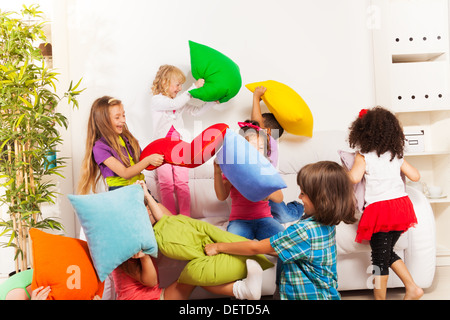 Pillow fight - large group of kids actively playing with pillow in the living room on the coach Stock Photo