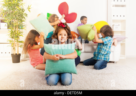 Happy smiling little Asian girl hugging pillow with large group of her friends pillow fighting on the background Stock Photo