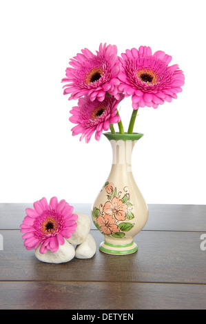 Pink Gerbera in decorated vase with pile of white stones on a dark brown wooden shelf Stock Photo