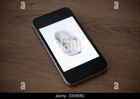 Modern mobile phone with fingerprint mark on a screen lying on brown wooden desk. Mobile security concept. Stock Photo