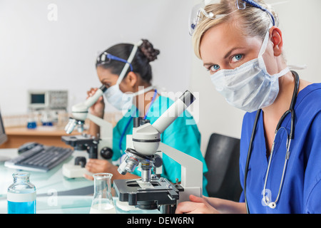 Blond female medical scientific researcher or doctor using microscope in laboratory with an Indian Asian colleague beside her Stock Photo