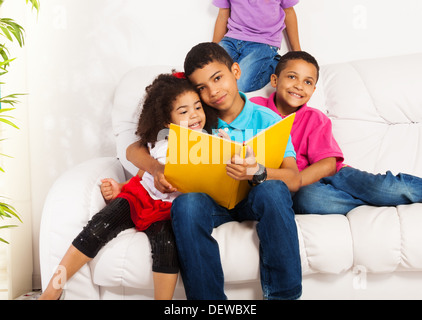 Family, group of four kids with older brother reading books to brothers and sister hugging little girl Stock Photo