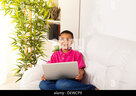 Cute 8 years old boy sitting on the sofa at home with laptop smiling.  Stock Photo