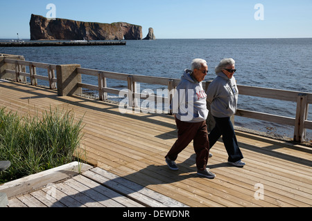 A couple walking on the boardwalk with Percé Rock in the background,  Percé Québec Canada Stock Photo