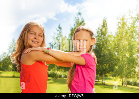 Portrait of two girls bright orange shirts holding hands together and dancing in the park on sunny day Stock Photo