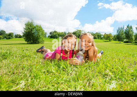 Two happy little nine years old girls hold jar with butterfly laying in the grass and showing big smile on happy faces  Stock Photo