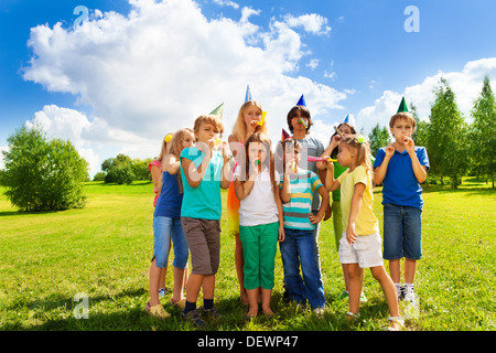 Large group of happy kids outside on a birthday party blowing noisemakers horns and twisted whistles Stock Photo