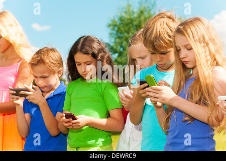 Group of busy kids looking at their phones texting sms and playing staying outside Stock Photo
