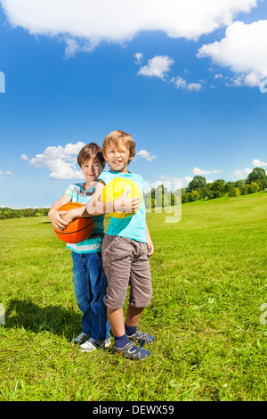 Two sibling boys stand with holding balls standing in the park on sunny summer day  Stock Photo