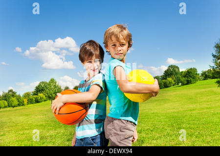 Two brothers stand with holding balls standing in the park on sunny summer day  Stock Photo