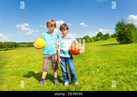 Two brothers boys kids stand with holding balls standing in the park on sunny summer day  Stock Photo