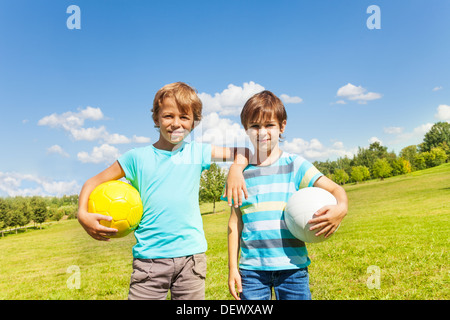 Portrait of two brothers boys stand with holding balls standing in the park on sunny summer day  Stock Photo