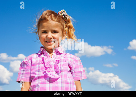 Nice smiling little 5 years old girl in pink shirt standing with sky on background Stock Photo