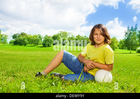 Portrait of 12 years old boy lay in the grass with basketball ball on the field on bright sunny day Stock Photo