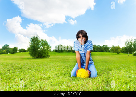 Portrait of 14 years old boy sit with soccer ball on the field on bright sunny day Stock Photo