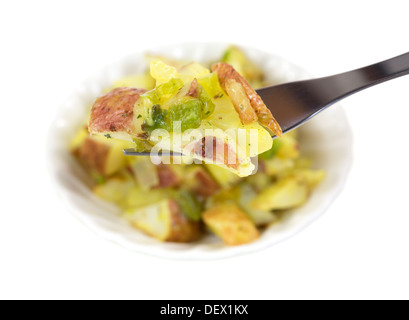 Roasted red potatoes with green peppers and onions on a fork with a small filled bowl blurred in the background. Stock Photo
