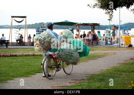 Man collecting PET bottles for recycling in big plastic bags and carrying them on a bike Stock Photo