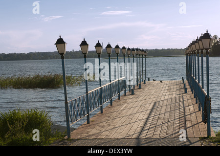 Long wooden dock leading into water, with lights on the edges Stock Photo