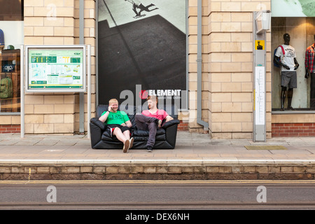 Two young men sitting on a sofa waiting for a tram in Nottingham city centre, England, UK Stock Photo
