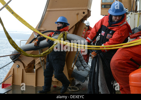 Seaman Aaron Lopez and Seaman Alex Cason, members of the Coast Guard Cutter Healy deck department, help handle the hose for an oil skimming?system during a simulated oil spill response exercise in the Arctic Ocean, Sept. 12, 2013. The crew of the Healy, a Stock Photo