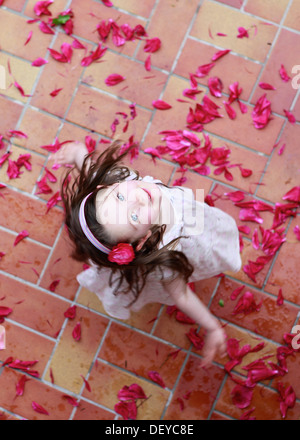 Little girl, three years, dancing on red petals, from above Stock Photo