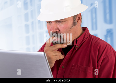 Hardhat worker perplexed, working on the tough issues with his laptop, he has a serious thoughtful look that he values his job Stock Photo
