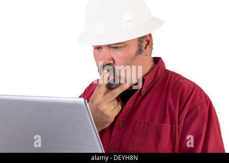 Hardhat worker working or surfing with his laptop, he has a puzzled look, he is wearing red shirt and isolated on white Stock Photo