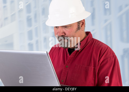 Hardhat worker working on the tough issues with his laptop, he has a serious thoughtful look that he values his job Stock Photo