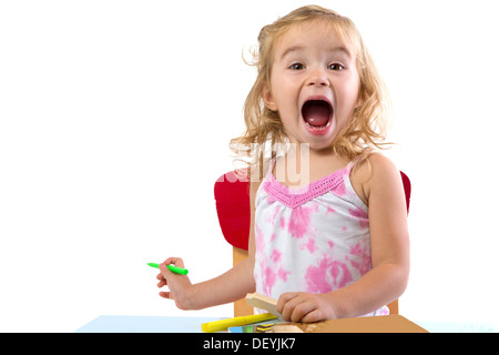 Toddler girl learning at the table very excited , her eyebrows are raised and mouth opened large holding colorful markers Stock Photo